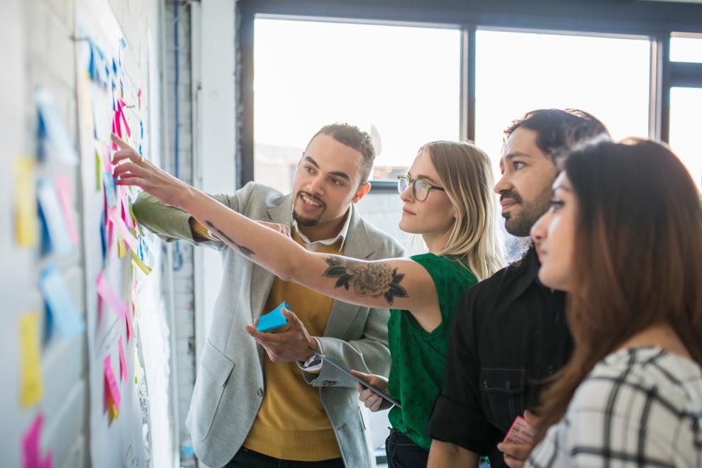 A group of 4 people are pointing to a white board with sticky notes on it.